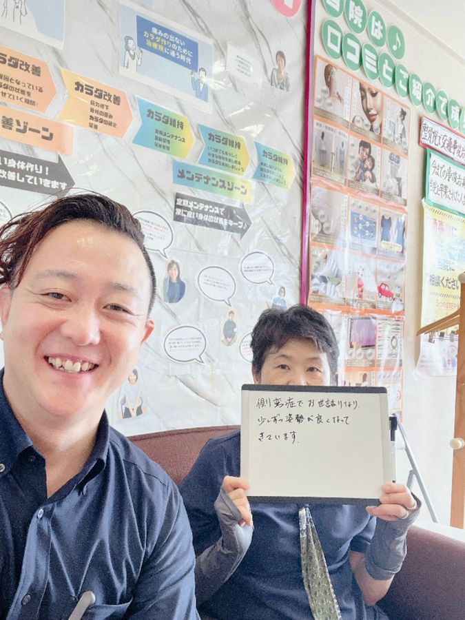 院長と女性の患者さん　ホワイトボードに「側弯症でお世話になり、少しずつ姿勢が良くなってきています」